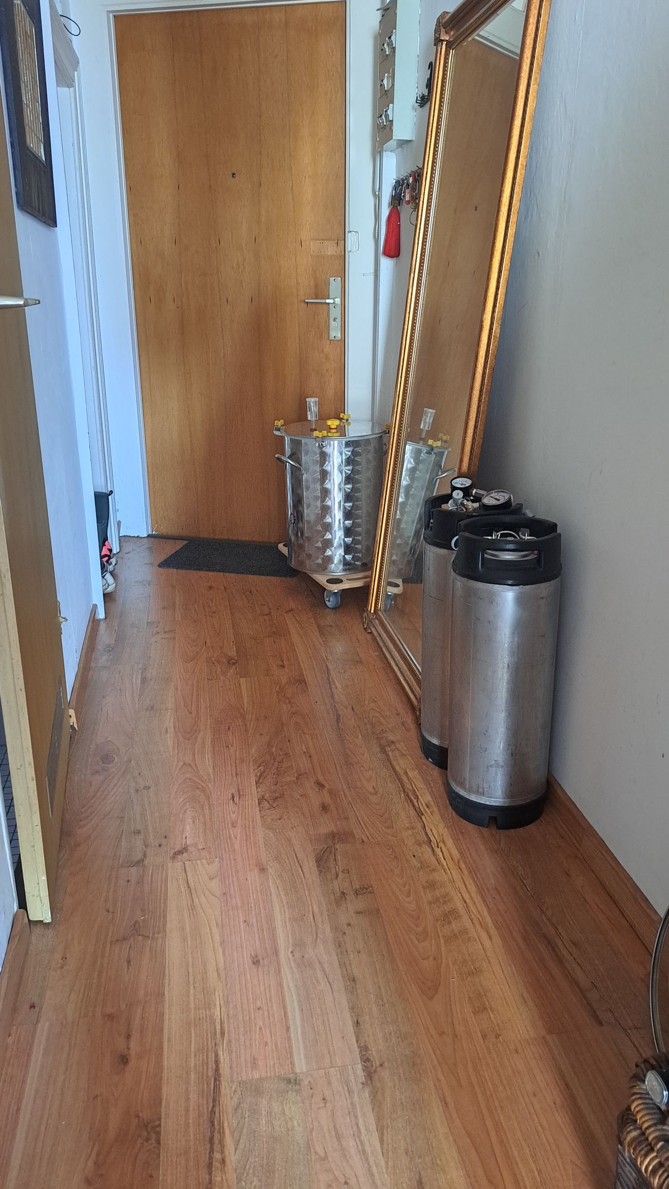 Wohnungsflur im Vordergrund zwei Kegfässer, dahinter lehnt ein hoher Spiegel an der Wand. Dahinter ein Gärtank aus Edelstahl